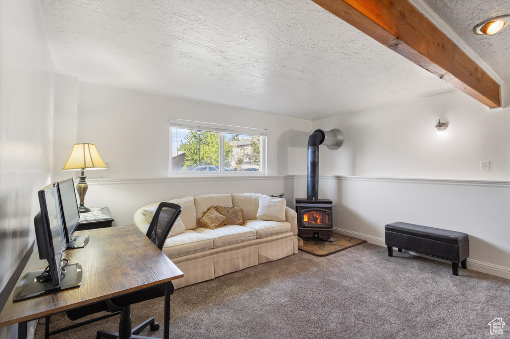 Carpeted office space featuring a wood stove, a textured ceiling, and baseboards
