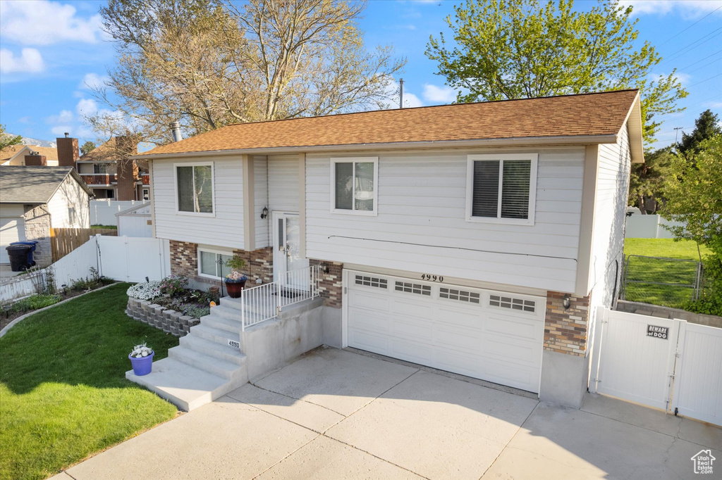 Split foyer home with fence, an attached garage, brick siding, driveway, and a front yard