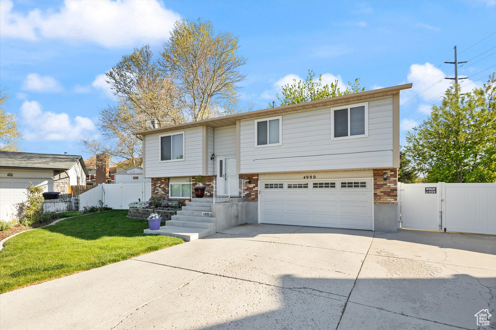 Bi-level home featuring a gate, fence, concrete driveway, a garage, and a front lawn