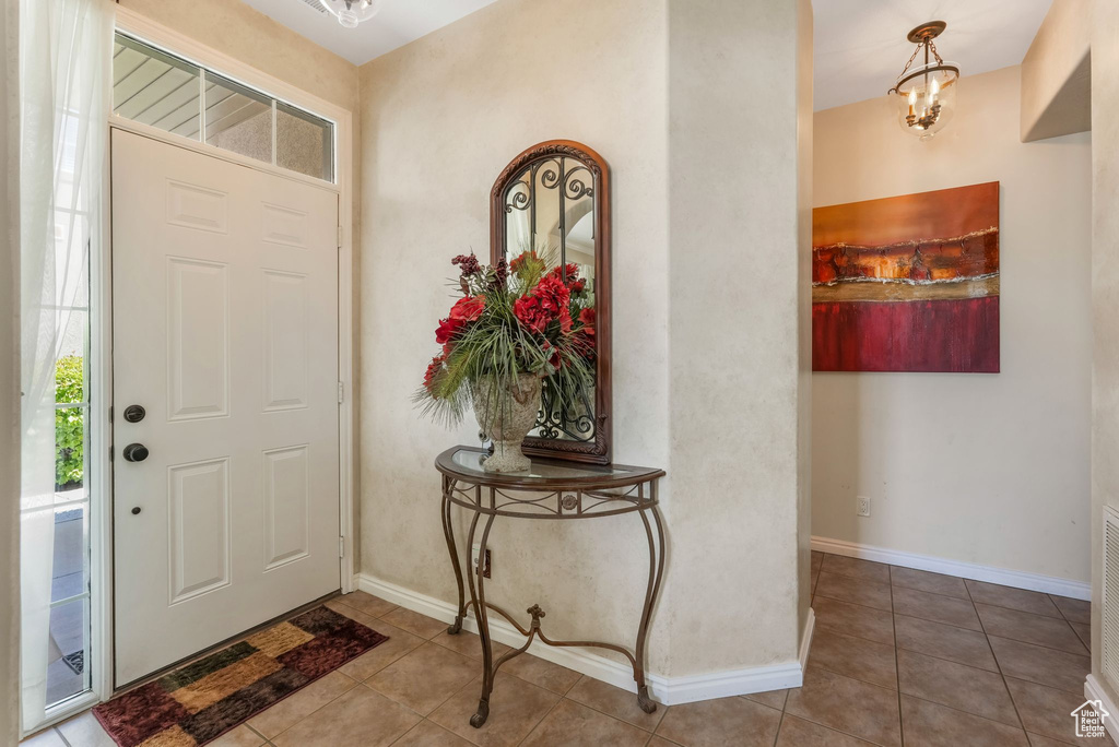 Tiled entryway with a chandelier and baseboards