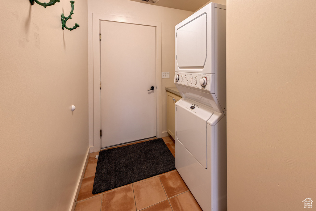 Laundry area featuring cabinet space, baseboards, light tile patterned flooring, and stacked washer and dryer