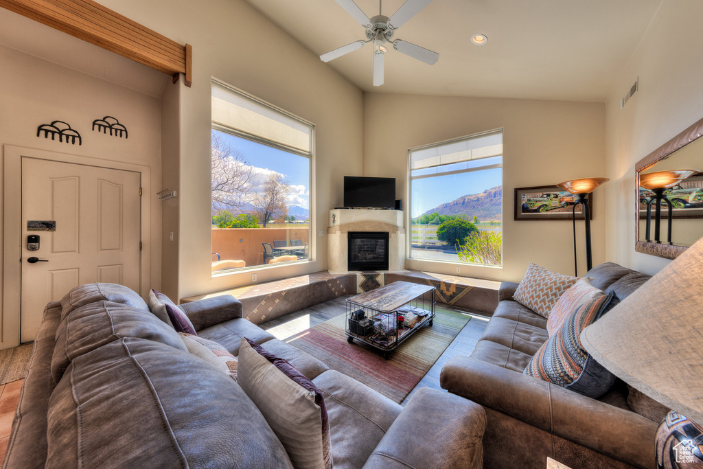 Living area featuring lofted ceiling, a glass covered fireplace, ceiling fan, and plenty of natural light