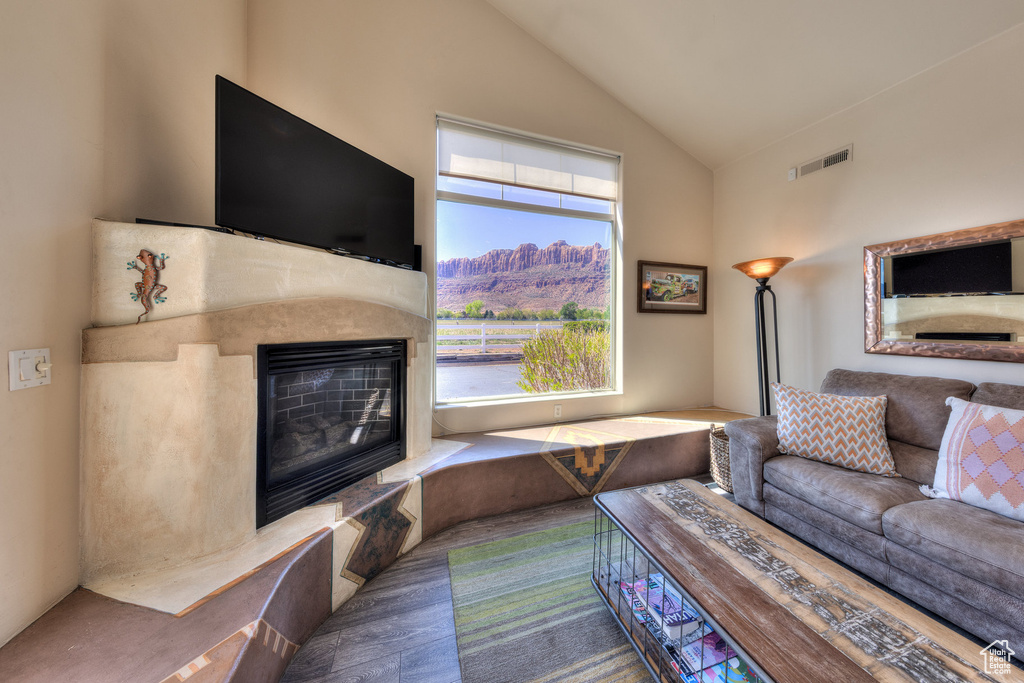Living room with high vaulted ceiling, visible vents, wood finished floors, and a high end fireplace