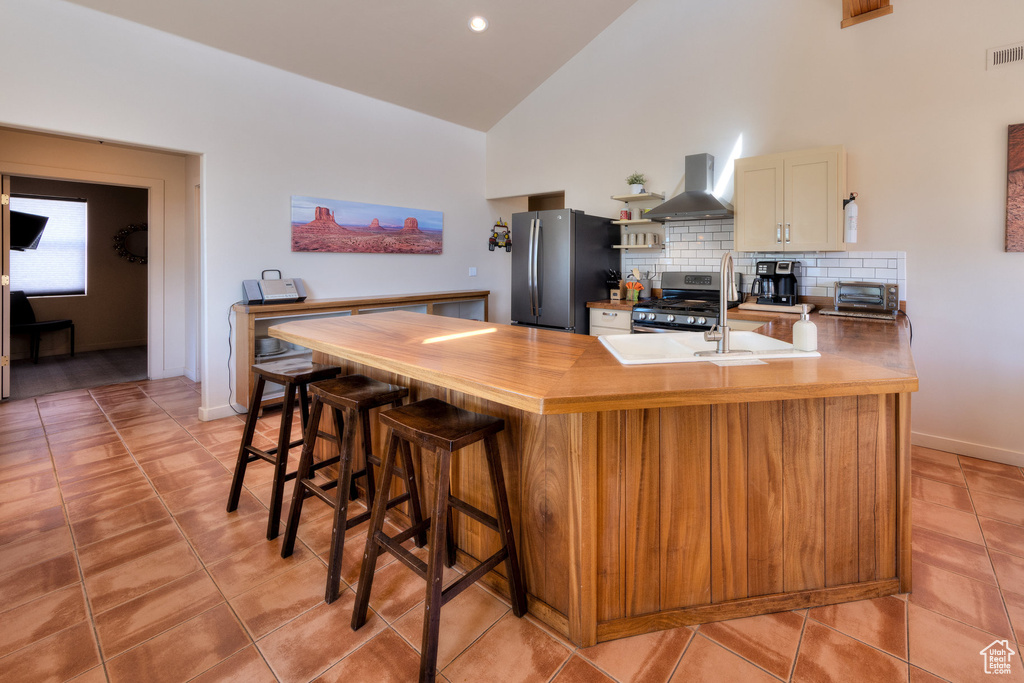 Kitchen featuring a peninsula, tasteful backsplash, high vaulted ceiling, wall chimney exhaust hood, and appliances with stainless steel finishes
