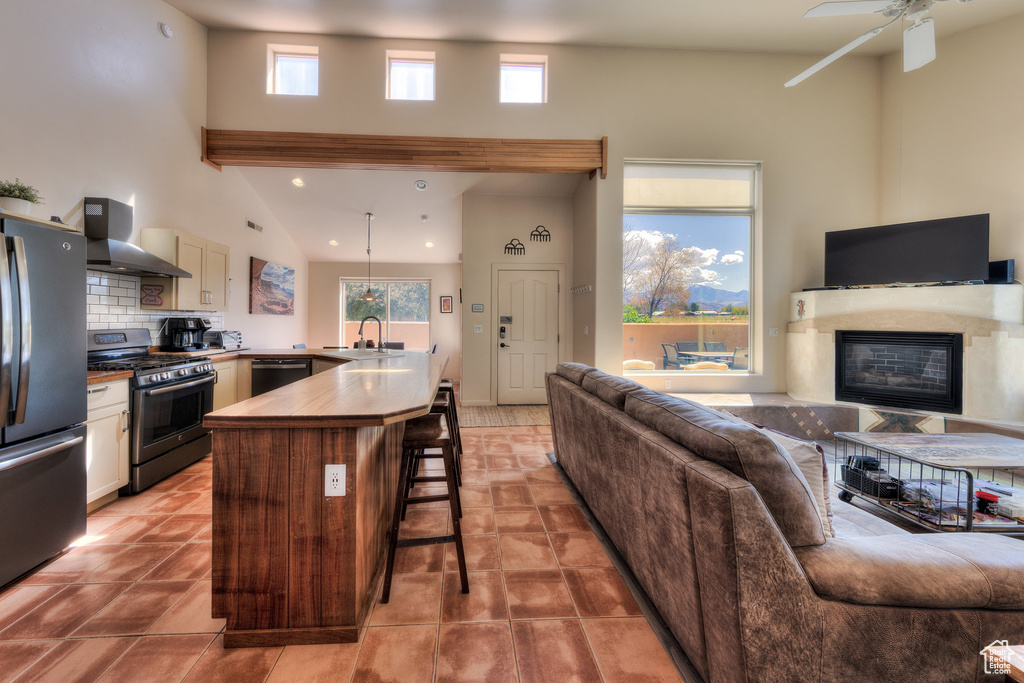 Kitchen featuring a kitchen bar, a sink, stainless steel appliances, open floor plan, and wall chimney range hood