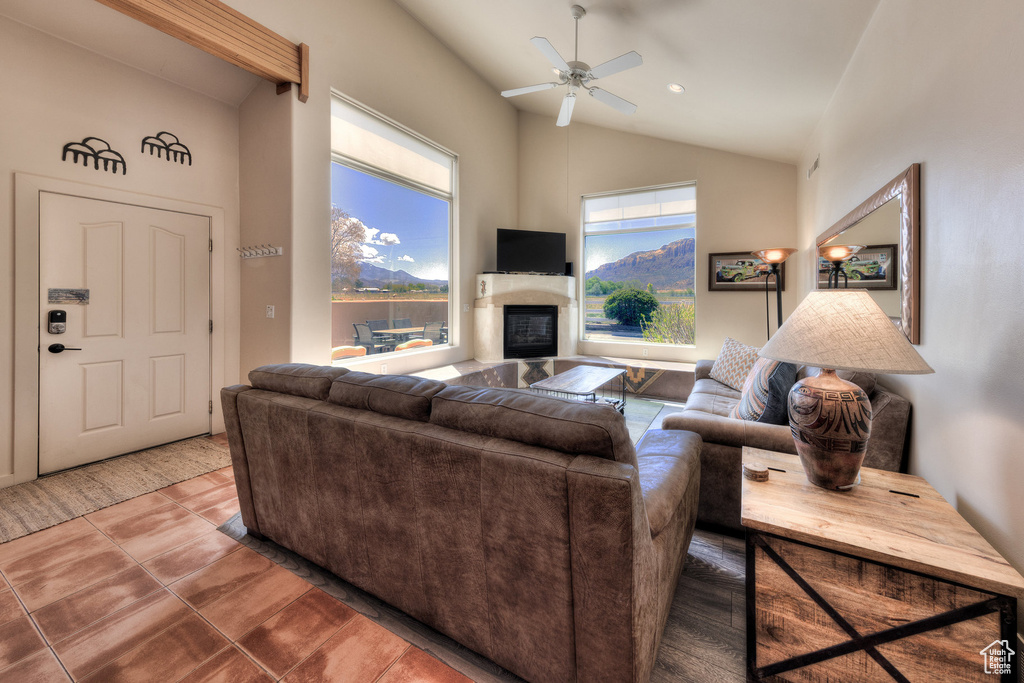 Living area featuring vaulted ceiling, tile patterned flooring, a ceiling fan, and a glass covered fireplace