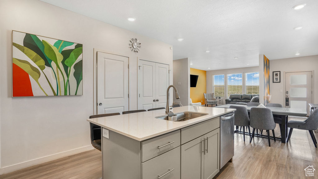 Kitchen with gray cabinets, stainless steel dishwasher, a sink, light countertops, and light wood-style floors