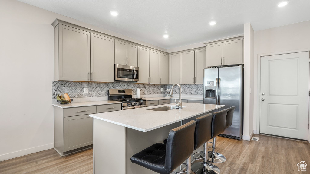 Kitchen with appliances with stainless steel finishes, a sink, light wood-style floors, backsplash, and gray cabinetry