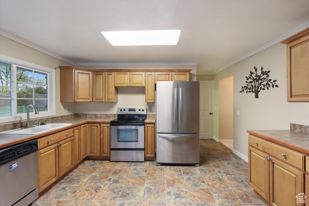 Kitchen featuring stone finish floor, a sink, crown molding, appliances with stainless steel finishes, and a skylight