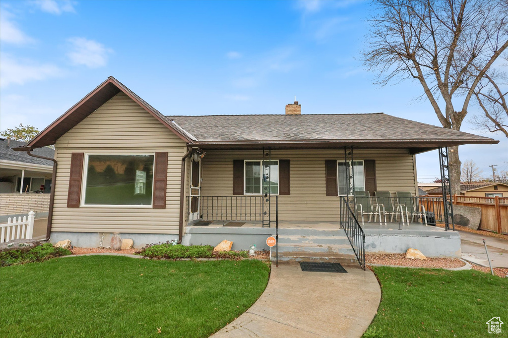 Ranch-style house featuring a chimney, a porch, a front lawn, and fence
