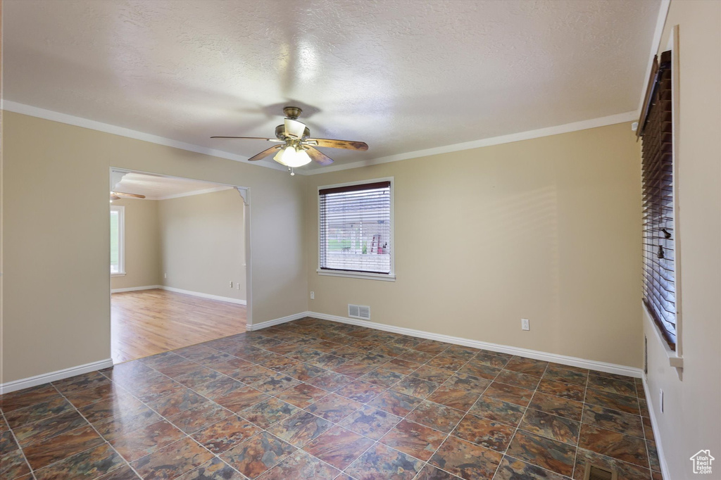Empty room with a textured ceiling, visible vents, baseboards, and ceiling fan