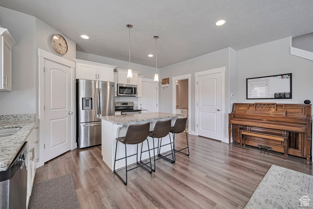 Kitchen with light stone countertops, a breakfast bar area, stainless steel appliances, white cabinetry, and wood finished floors