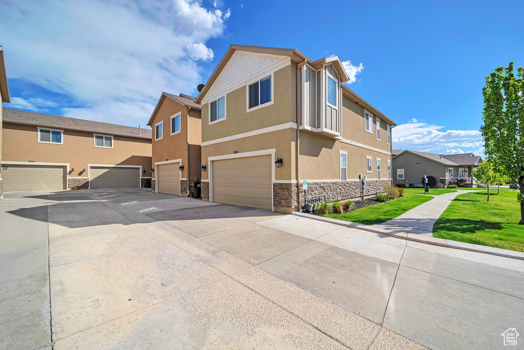 Exterior space with driveway, a residential view, an attached garage, stone siding, and stucco siding