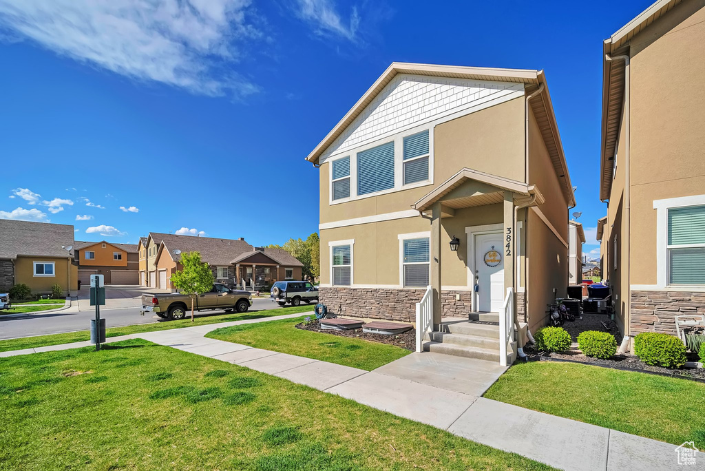 View of front of property with a residential view, stucco siding, a front lawn, and stone siding