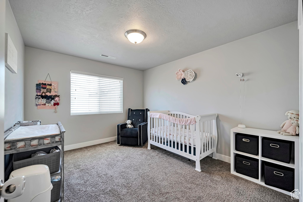 Carpeted bedroom featuring visible vents, a textured ceiling, baseboards, and a nursery area