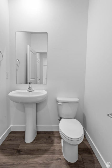 Half bath with baseboards, toilet, and wood finished floors