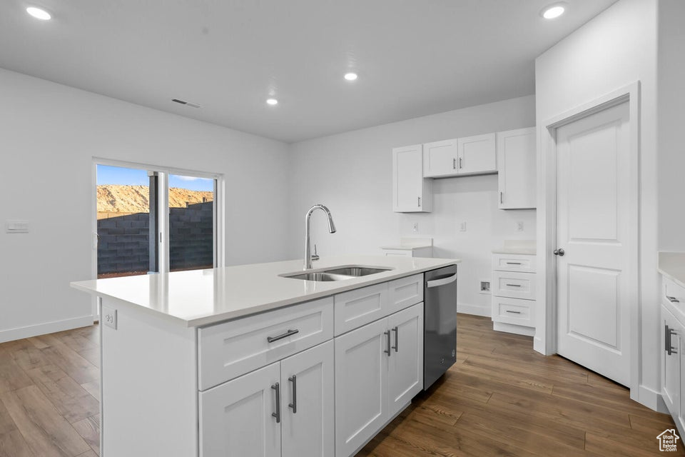Kitchen featuring a sink, dark wood finished floors, an island with sink, dishwasher, and white cabinets
