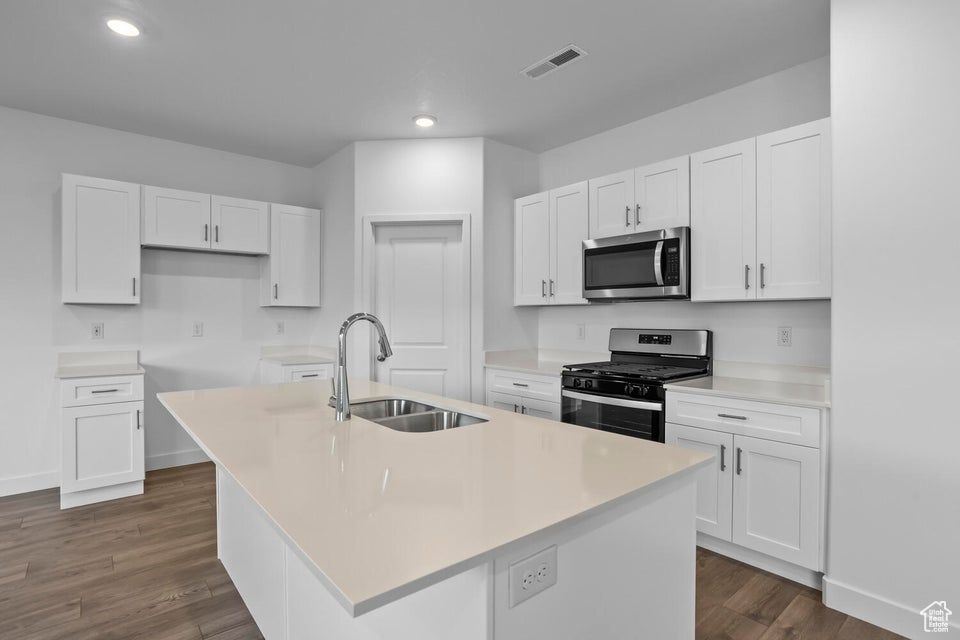 Kitchen with stainless steel appliances, white cabinets, an island with sink, and a sink