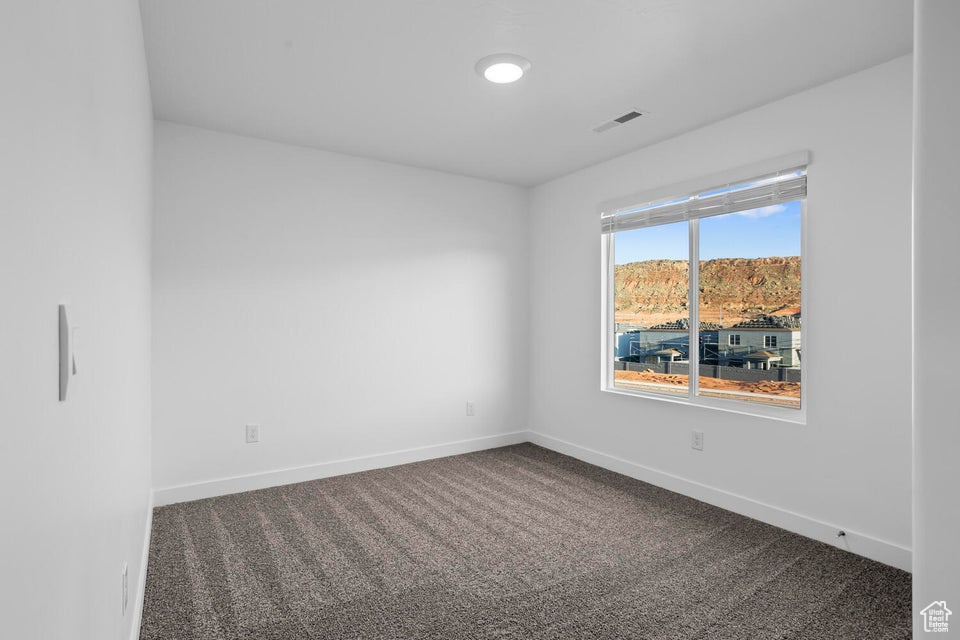 Unfurnished room featuring baseboards, dark colored carpet, and visible vents