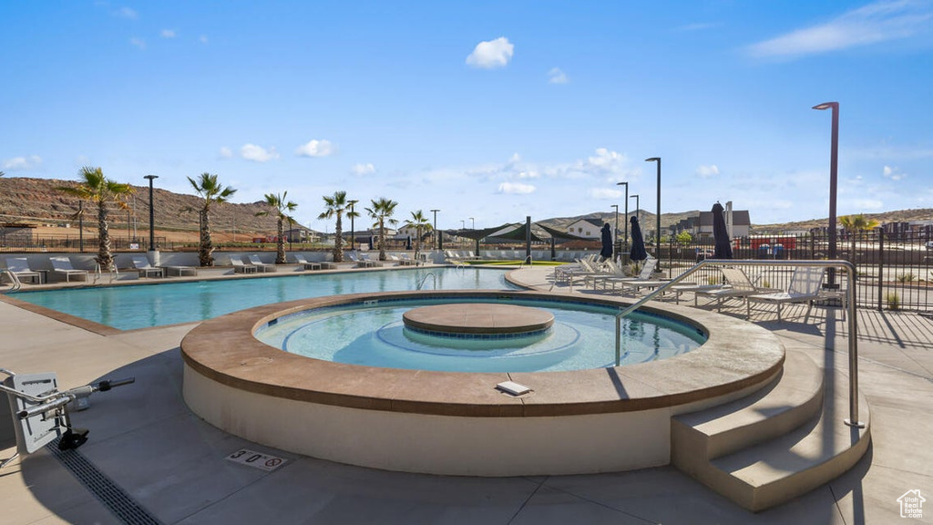 Community pool with a patio, a hot tub, and fence