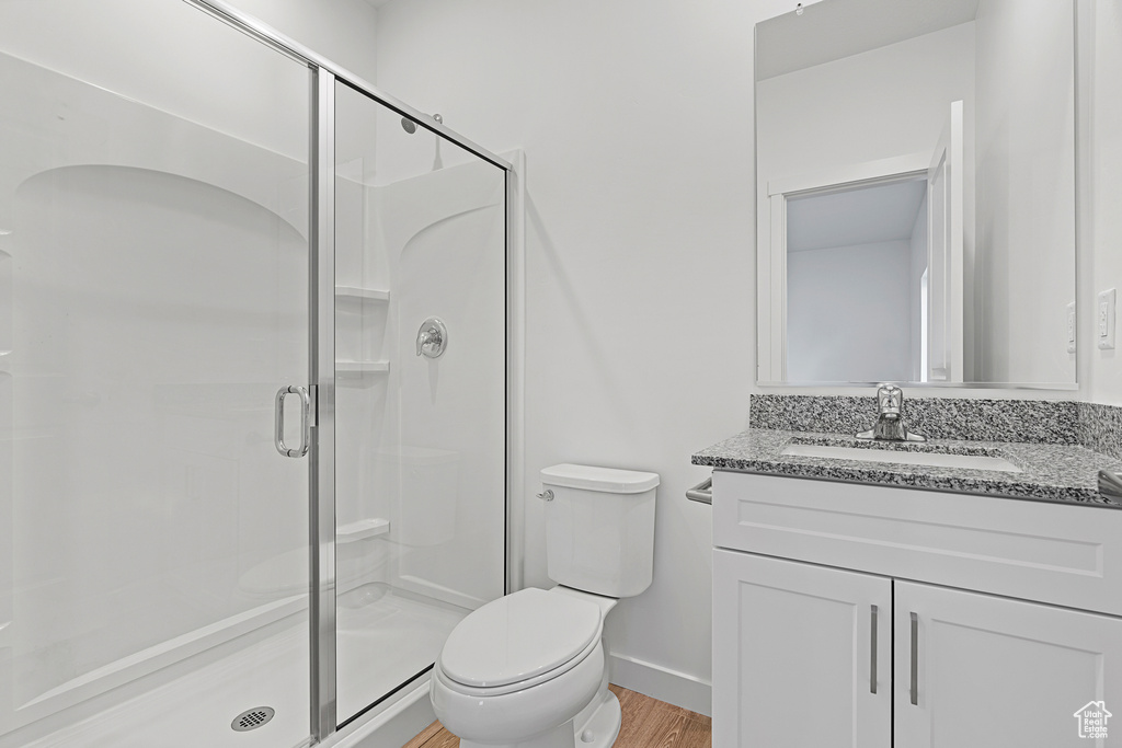 Full bath with toilet, wood finished floors, a stall shower, baseboards, and vanity