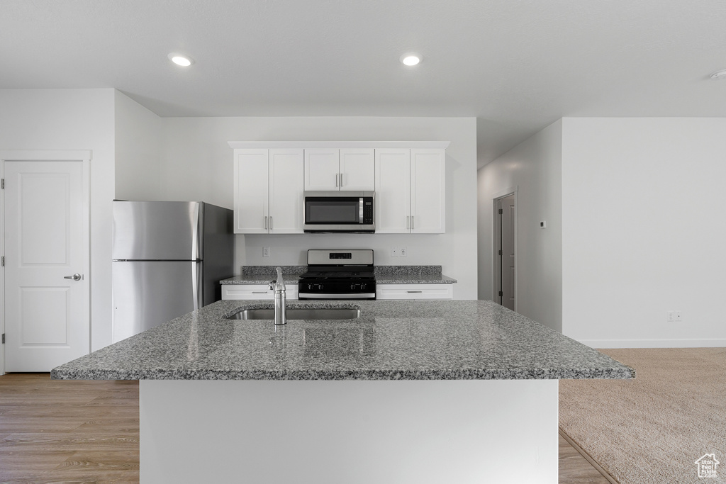 Kitchen featuring a sink, dark stone counters, a center island with sink, white cabinets, and appliances with stainless steel finishes