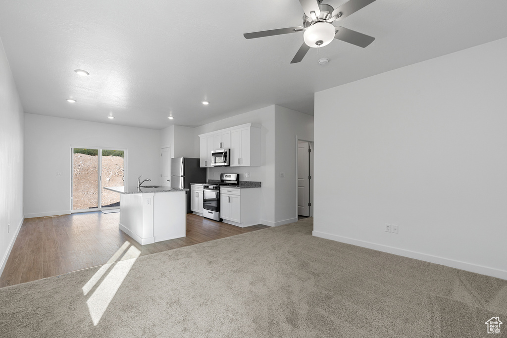 Kitchen with a ceiling fan, stainless steel appliances, a kitchen island with sink, white cabinetry, and baseboards