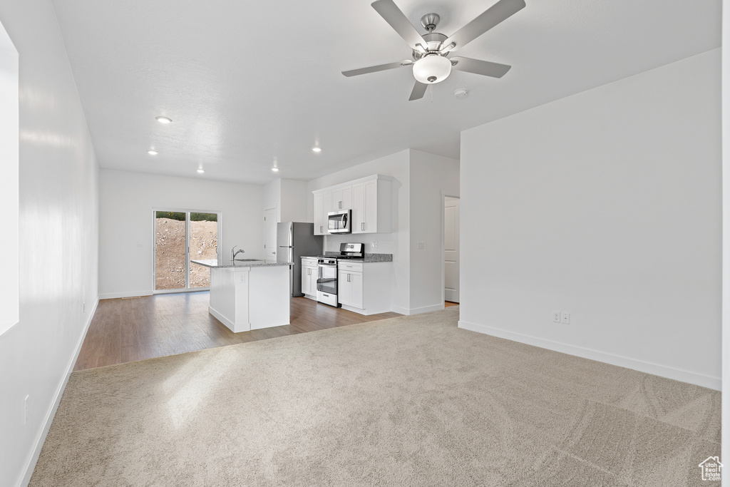 Unfurnished living room featuring a sink, carpet, recessed lighting, a ceiling fan, and baseboards