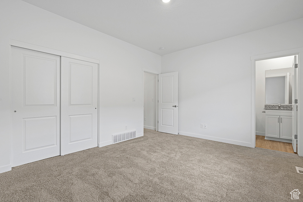 Unfurnished bedroom with a closet, light colored carpet, ensuite bath, visible vents, and baseboards