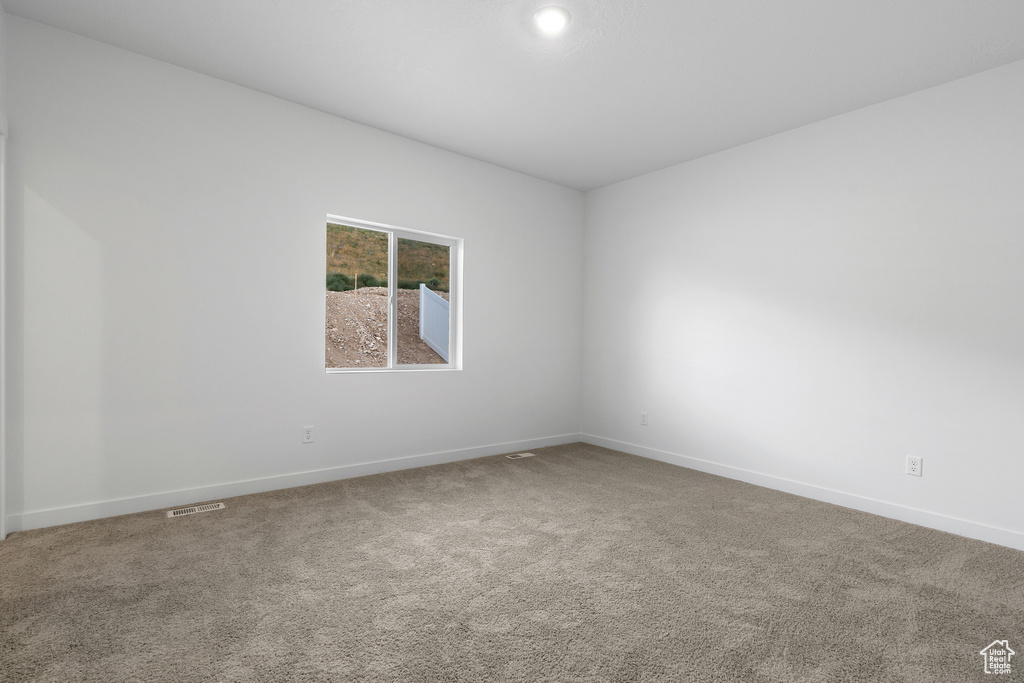 Empty room with carpet flooring, visible vents, and baseboards
