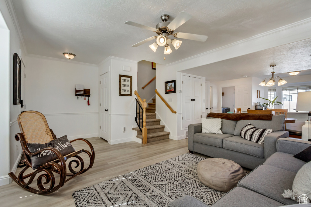 Living area featuring light wood-style flooring, stairs, ceiling fan with notable chandelier, and baseboards