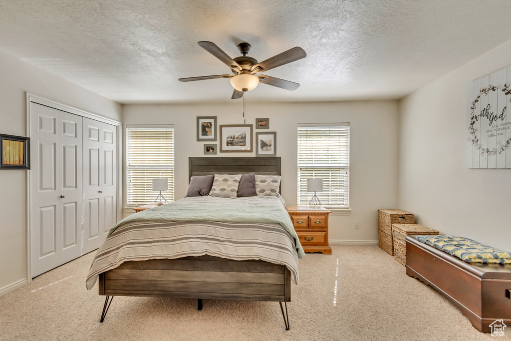 Carpeted bedroom with baseboards, a textured ceiling, a closet, and a ceiling fan