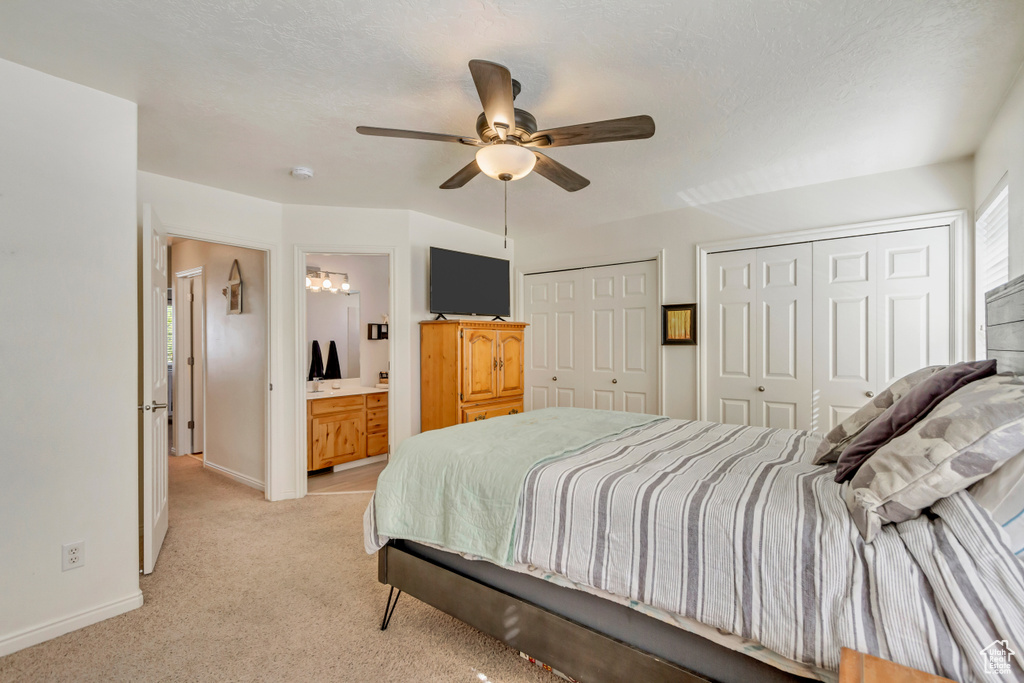 Bedroom with a ceiling fan, baseboards, ensuite bath, multiple closets, and light colored carpet
