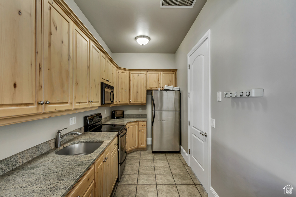 Kitchen featuring light brown cabinetry, light stone countertops, light tile patterned floors, a sink, and appliances with stainless steel finishes