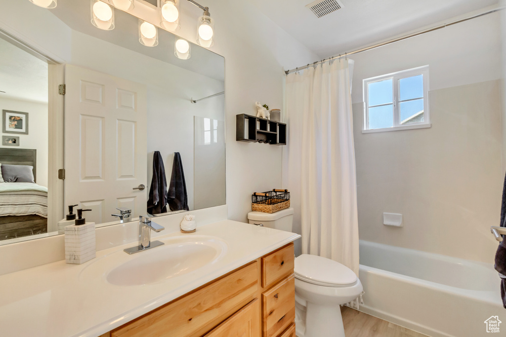 Ensuite bathroom with toilet, wood finished floors, shower / tub combo, visible vents, and vanity