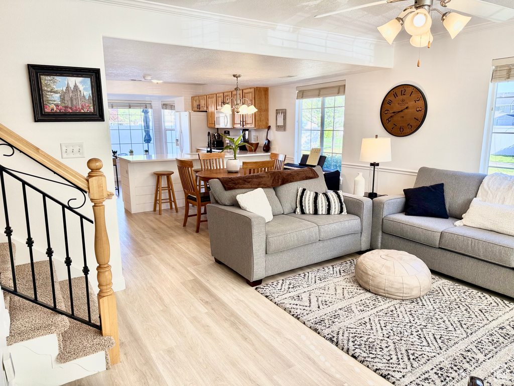 Living area featuring ornamental molding, light wood finished floors, stairway, and ceiling fan with notable chandelier