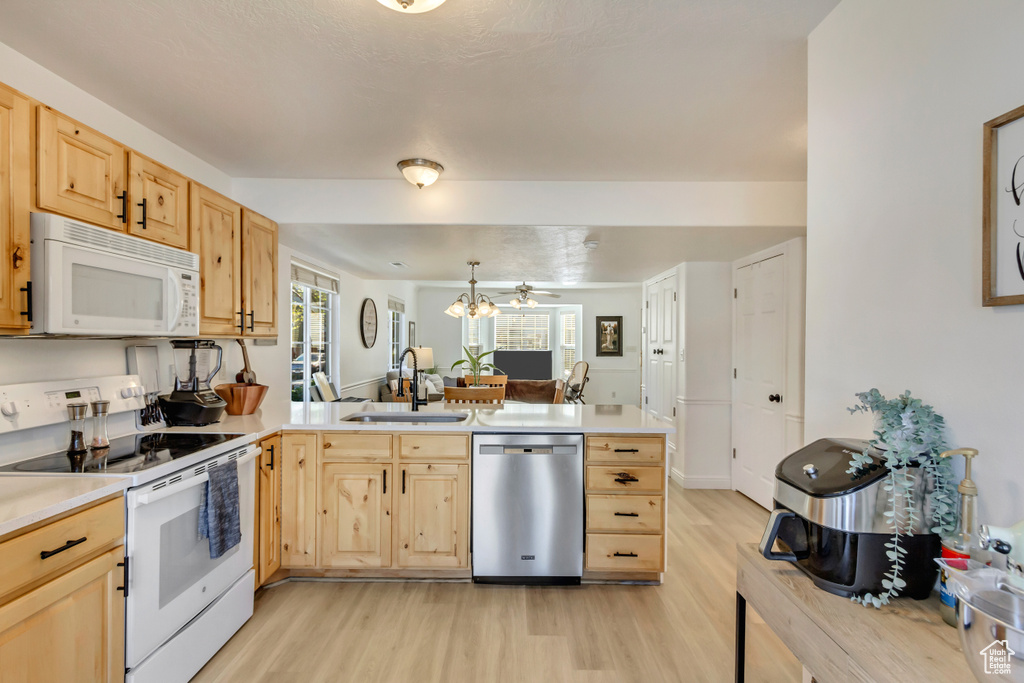 Kitchen featuring light brown cabinets, white appliances, a sink, a peninsula, and light wood-style floors