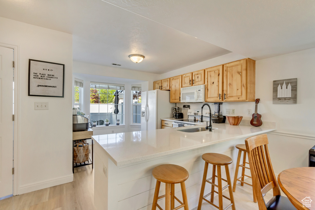 Kitchen featuring a breakfast bar area, white appliances, a sink, a peninsula, and light countertops
