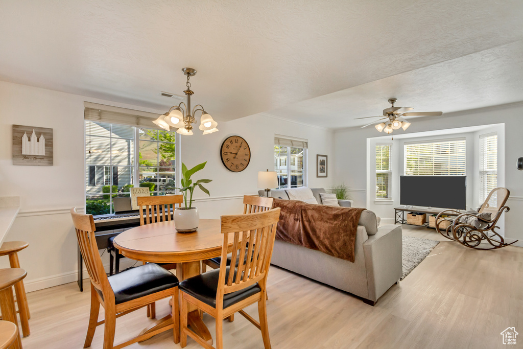 Dining area featuring light wood finished floors, visible vents, and ceiling fan with notable chandelier