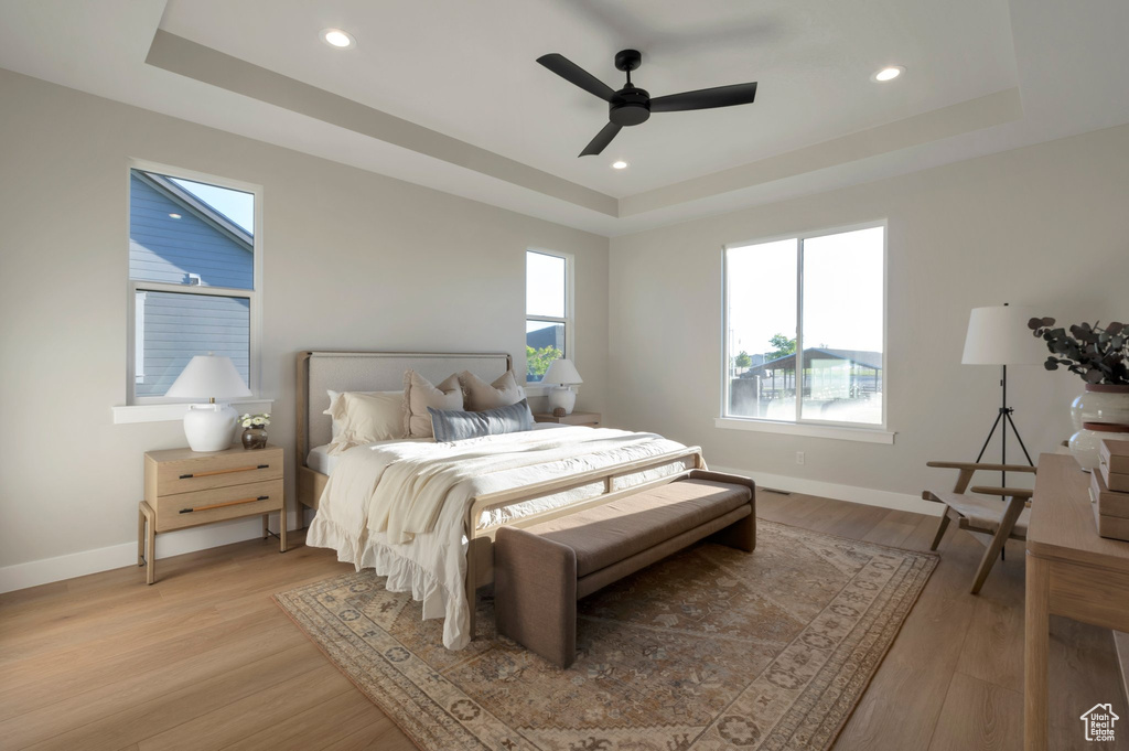 Bedroom featuring a ceiling fan, a tray ceiling, recessed lighting, baseboards, and light wood-style floors