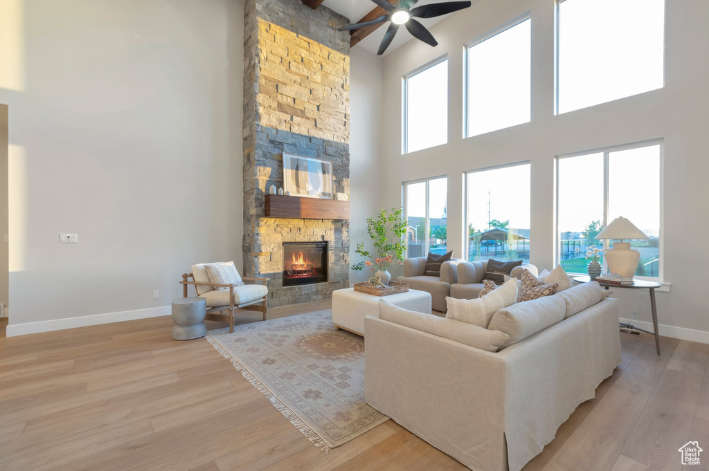 Living area with light wood finished floors, a ceiling fan, a high ceiling, baseboards, and a stone fireplace