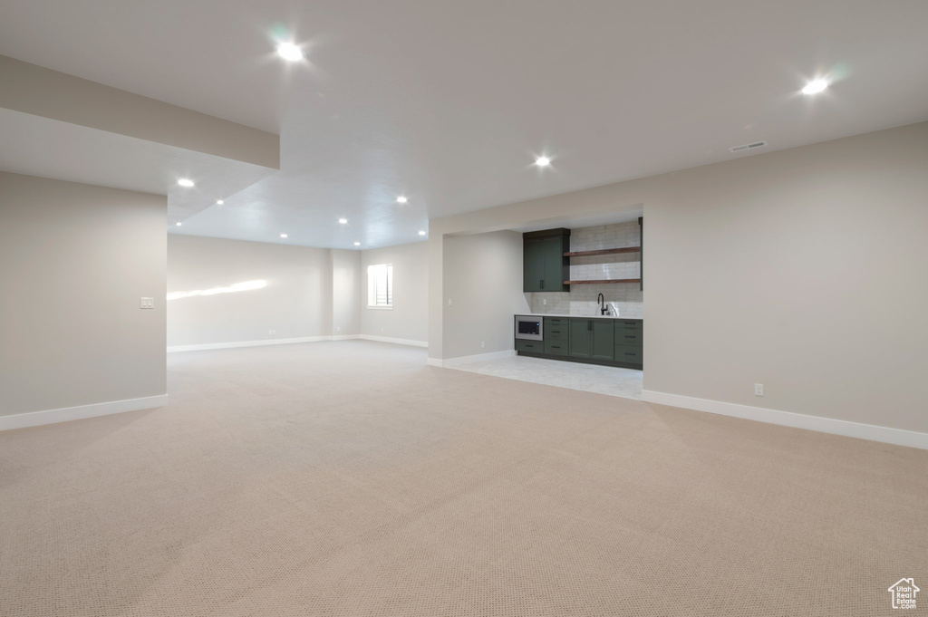 Unfurnished living room featuring a sink, light colored carpet, baseboards, and recessed lighting