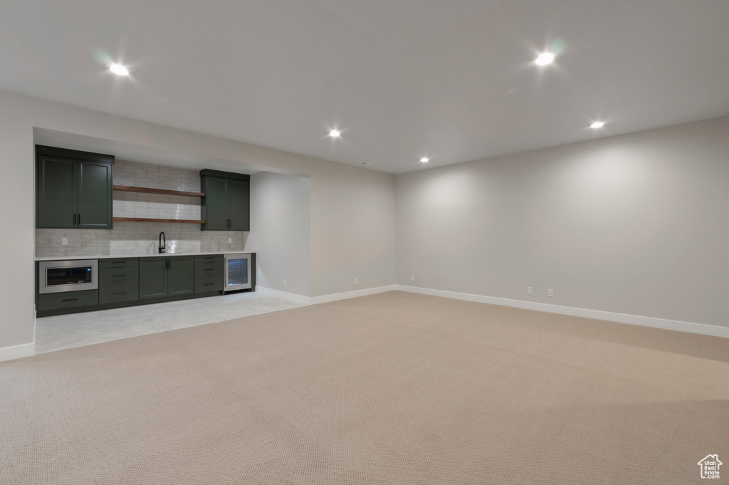 Unfurnished living room featuring wine cooler, recessed lighting, baseboards, indoor wet bar, and light colored carpet