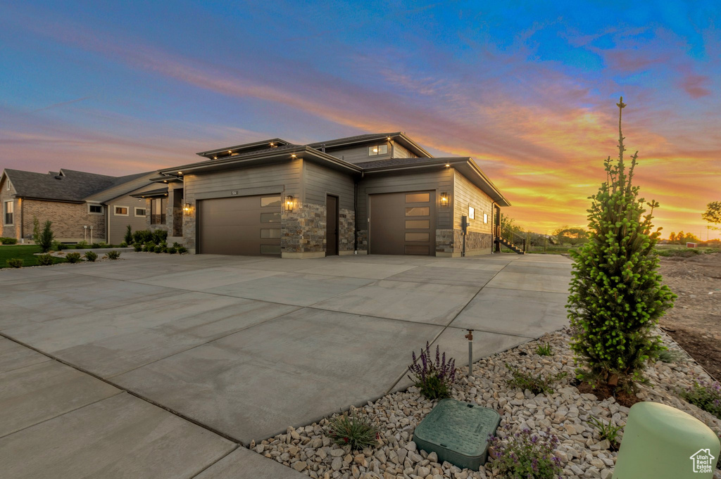 Prairie-style house featuring stone siding, roof mounted solar panels, driveway, and a garage