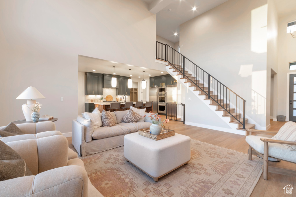 Living area with baseboards, stairs, light wood-style flooring, and a towering ceiling