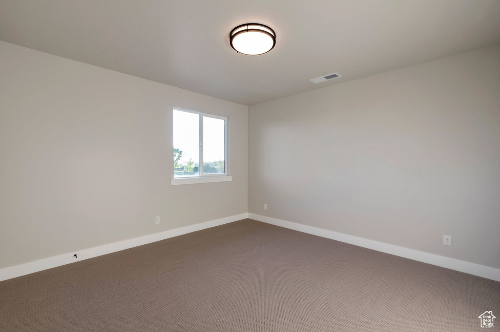 Spare room featuring visible vents, baseboards, and dark colored carpet