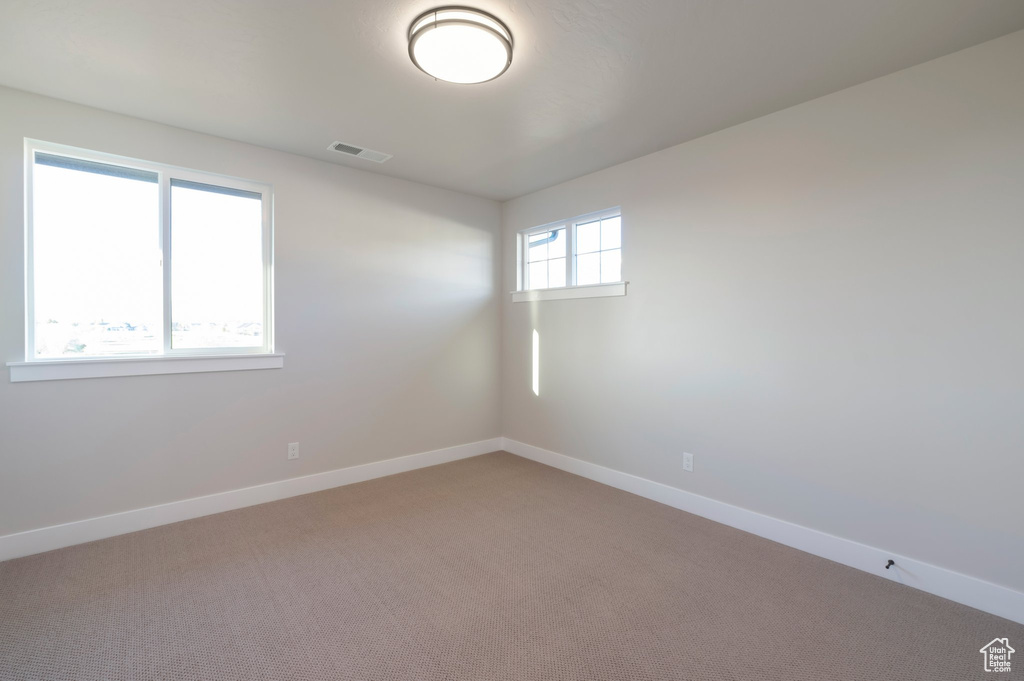 Empty room featuring baseboards, visible vents, and light colored carpet