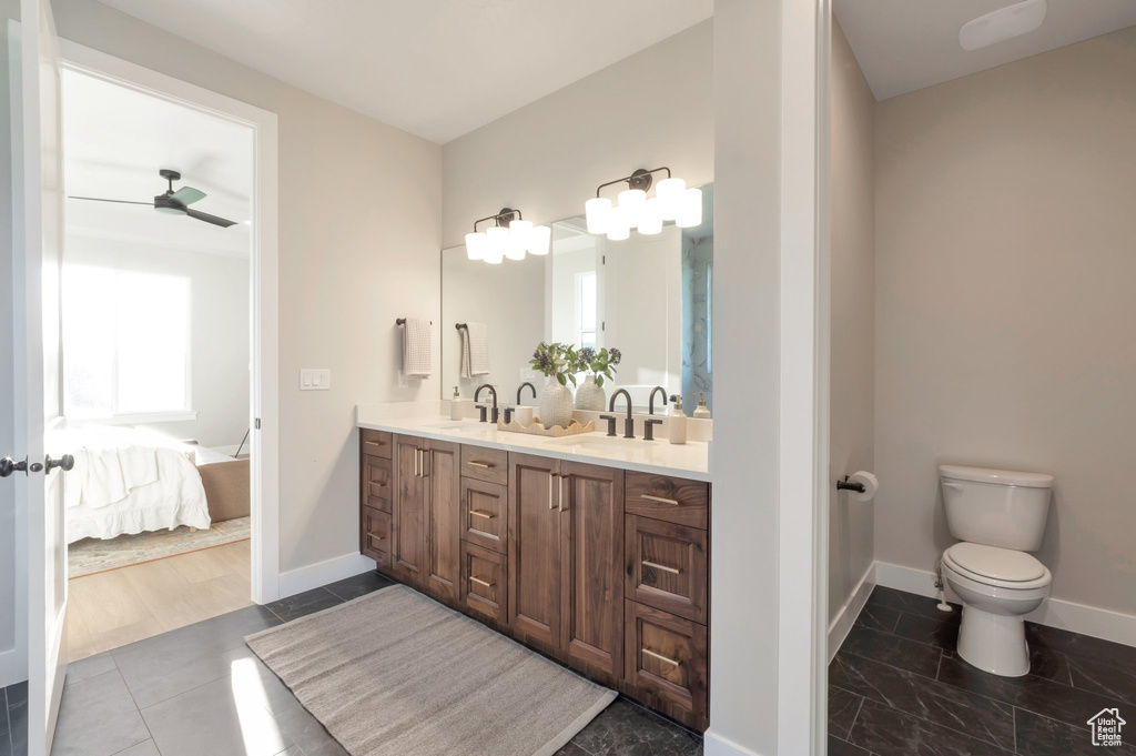 Ensuite bathroom featuring double vanity, connected bathroom, toilet, a sink, and baseboards