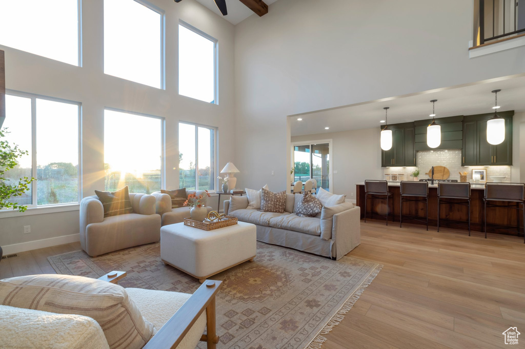 Living room with baseboards, ceiling fan, light wood-type flooring, and a high ceiling