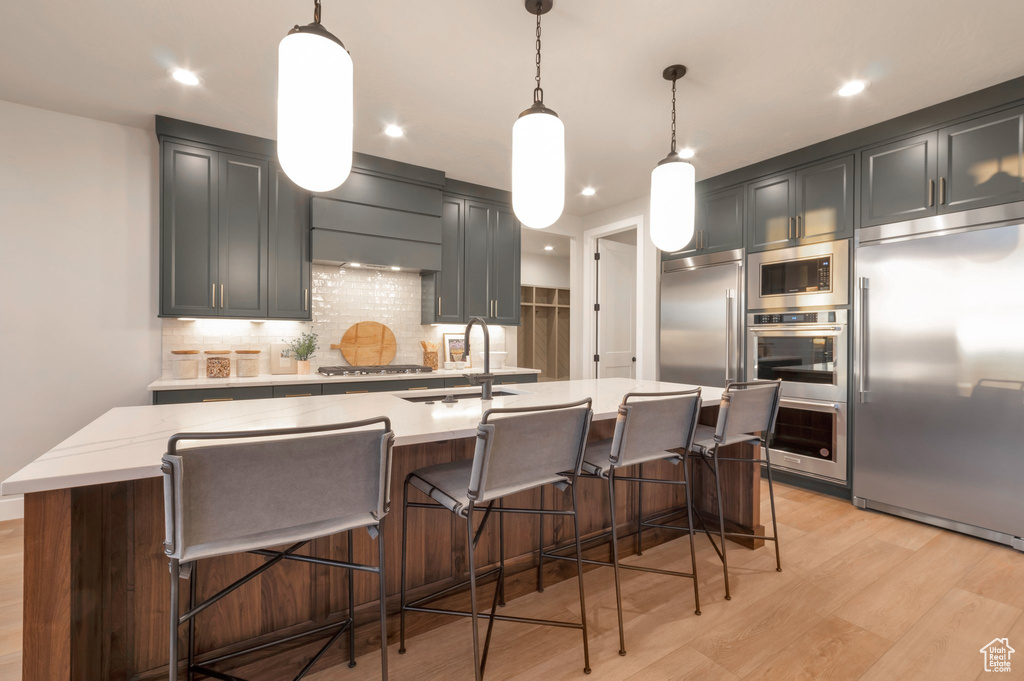 Kitchen with built in appliances, a sink, a kitchen breakfast bar, light wood-style floors, and tasteful backsplash